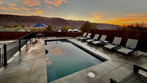 A swimming pool with lounge chairs and a view of a mountainous landscape during sunset. - Moab Desert Escape Villa: Luxury 5-Bedroom Retreat with Heated Pool (Moab)
