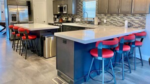 A modern kitchen with a central island, stainless steel appliances, and red bar stools. - Moab Desert Escape Villa: Luxury 5-Bedroom Retreat with Heated Pool (Moab)