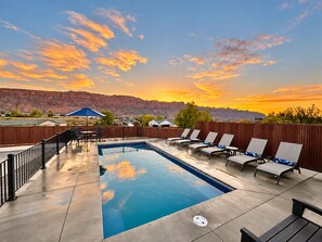 A swimming pool with lounge chairs and a view of a mountain range during sunset.