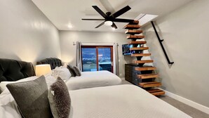 A modern bedroom with two beds, a ceiling fan, a TV, and a view of the outdoors through a sliding door. - Moab Desert Escape Villa: Luxury 5-Bedroom Retreat with Heated Pool (Moab)