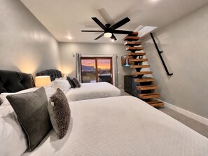 Een slaapkamer met twee bedden, een plafondventilator, een televisie en een trap.