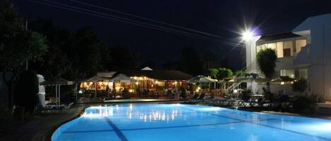 A swimming pool at night with a building in the background.