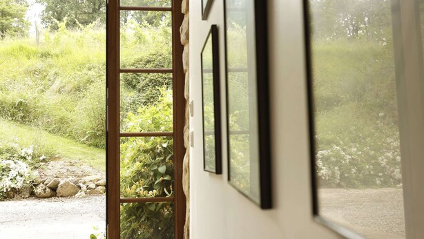 Vista attraverso una finestra con un muro di pietra e vegetazione all'esterno.
