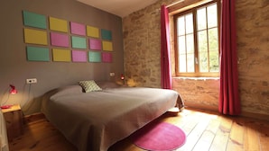 Una camera da letto con un letto, una finestra con tende, un muro decorato con opere d'arte colorate e un pavimento in legno.