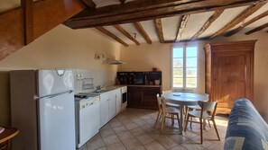 Une cuisine compacte équipée d’un réfrigérateur, d’une cuisinière et d’un four à micro-ondes. On y trouve une table à manger avec des chaises et un buffet en bois.
