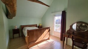 Une chambre à coucher avec un lit en bois, une table de chevet avec une lampe, une commode avec un miroir et une fenêtre avec des rideaux.