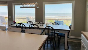 Un espace repas avec vue sur la plage, de grandes fenêtres et un luminaire suspendu.