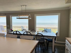 Un espace repas avec vue sur la plage, de grandes fenêtres et un luminaire suspendu.