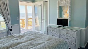 Une chambre à coucher comprenant un lit, une commode, un téléviseur et une grande fenêtre donnant sur la plage.