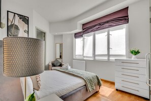 A modern bedroom with a bed, bedside table, lamp, window with curtains, and a dresser.