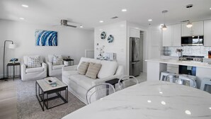 A modern living room with a white sofa, a coffee table, and a dining area with a marble table. - Private Beach, Pickleball, Tennis 3 heated pools! (Santa Rosa Beach)