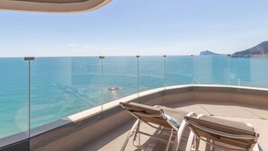 Un balcón con dos sillones de descanso que da a un mar azul y montañas lejanas.