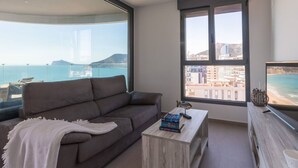 Una sala de estar moderna con un ventanal que ofrece vista al mar y edificios.