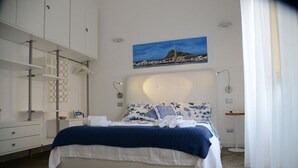 Une chambre à coucher moderne avec un grand lit, un tableau représentant un paysage côtier et des étagères intégrées.