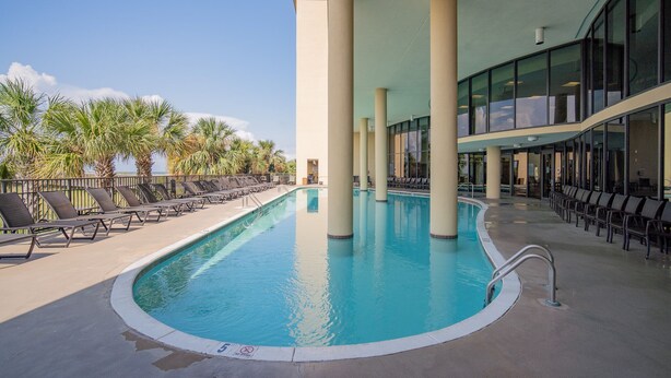 A swimming pool with lounge chairs and palm trees, surrounded by a building with large windows and columns.