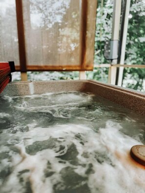 Ett bubbelbad med vatten, en träkonstruktion och ett fönster med grönska utanför.