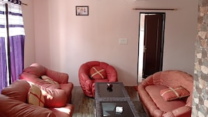 A living room with red sofas, a glass coffee table, and a stone accent wall. - Achal's जंगल में मंगल (Gurugram)
