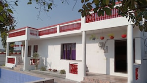 A two-story building with a red and white exterior, a balcony with red railings, and a small pool area. - Achal's जंगल में मंगल (Gurugram)