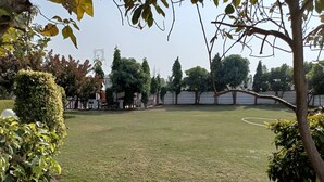 A well-maintained grassy area with a variety of trees and shrubs, surrounded by a low wall. - Achal's जंगल में मंगल (Gurugram)