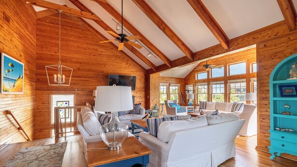 A spacious log cabin interior with a large sofa, a dining table, and a blue accent wall. - Shore Enough - Duck, Sanderling, 50 Yds to Beach, Elevator, Pets OK, Community Pool, Flex Stays (Duck)