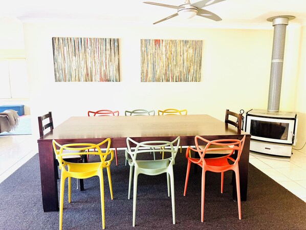 Un comedor con una mesa de madera y sillas coloridas, un ventilador de techo y una chimenea.