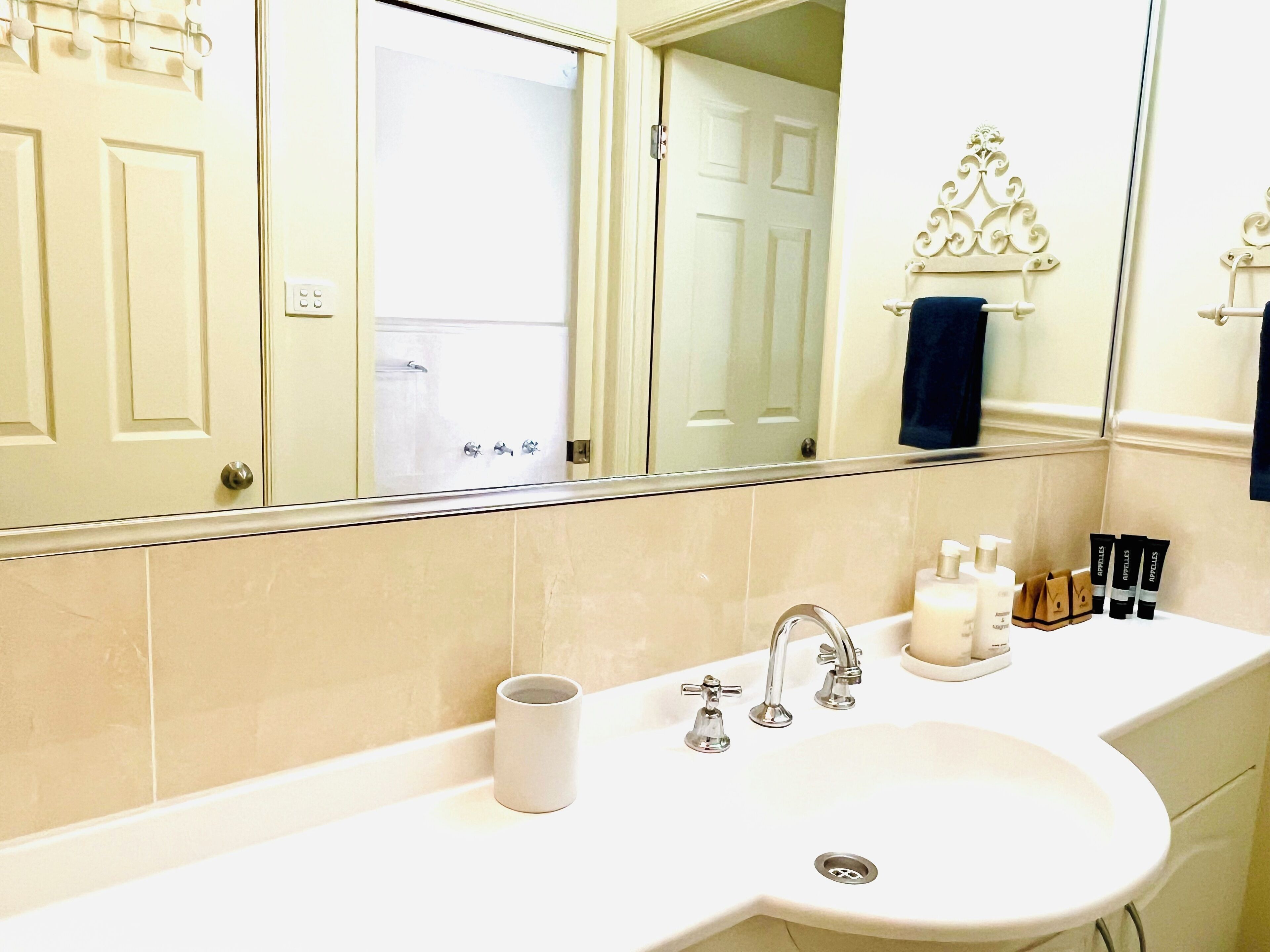 Une salle de bain avec un lavabo blanc, deux robinets, un miroir et des articles de toilette posés sur le comptoir.
