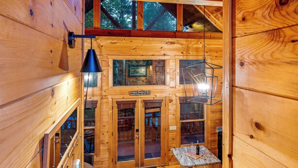 Interior de una cabaña de madera con comedor, escalera y vistas al exterior.