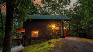 Une cabane rustique avec des fondations en pierre, un revêtement extérieur en bois et une véranda dotée d’une balustrade rouge.