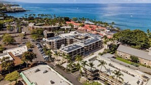 An aerial view of a coastal area with a large building featuring multiple floors and a flat roof with solar panels.