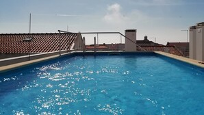 A rooftop swimming pool with clear blue water, surrounded by a tiled roof and a clear sky.