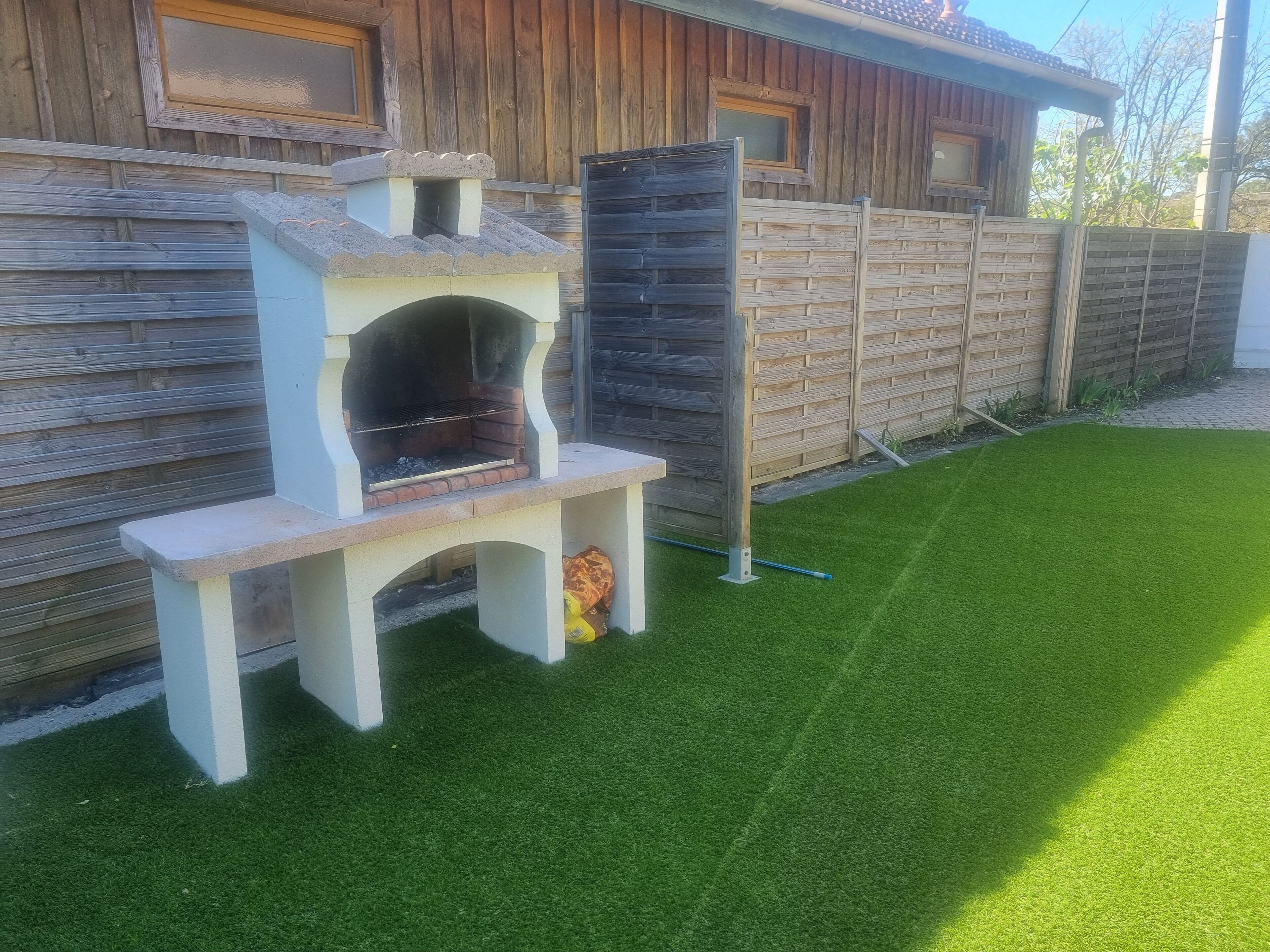 Een achtertuin met een ingebouwde barbecue, een houten omheining en kunstgras.