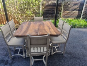 A wooden dining table with four chairs, surrounded by a garden with a wooden fence and greenery.