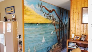 A room with a large painting of a sunset over the sea, a wooden wall, a bookshelf, and a door with a refrigerator. - Entire house 10 metres from the beach (Lège-Cap-Ferret)