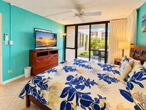 A bedroom with a bed, a television, a ceiling fan, and a view of the outside. - Kamaole Sands #9-111 Family-Friendly Suite Near Famous Kamaole III Beach (Kihei)