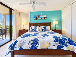 Een hotelkamer met een bed, twee bedlampjes, een plafondventilator, een raam met gordijnen en een schilderij aan de muur.