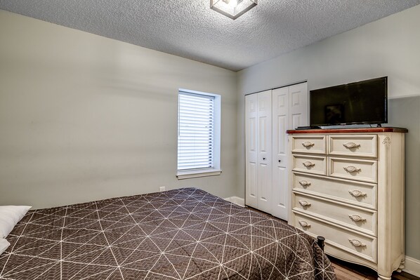 A bedroom with a bed, a dresser, a television, and a window with blinds.