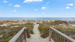 Une promenade en bois qui mène à une plage, avec un ciel dégagé.
