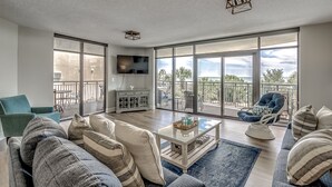 Un salon spacieux doté d’une grande porte-fenêtre donnant sur un balcon, d’un canapé confortable, d’une table basse et d’un téléviseur fixé au mur.
