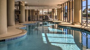 Une piscine intérieure à l’eau claire, entourée de piliers de couleur beige et de grandes fenêtres.