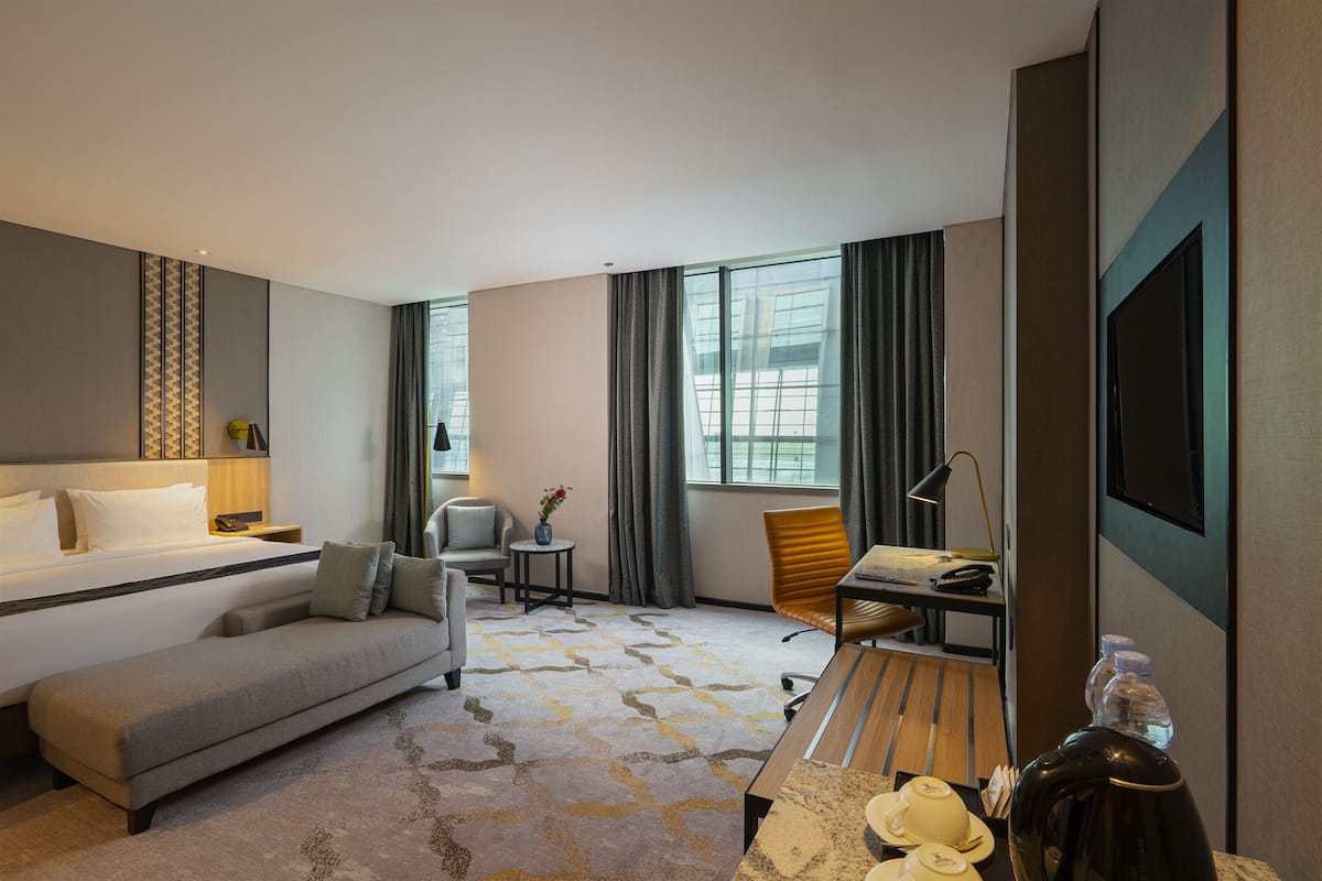 A hotel room with a bed, a sofa, a desk with a chair, a TV, and a window with curtains.