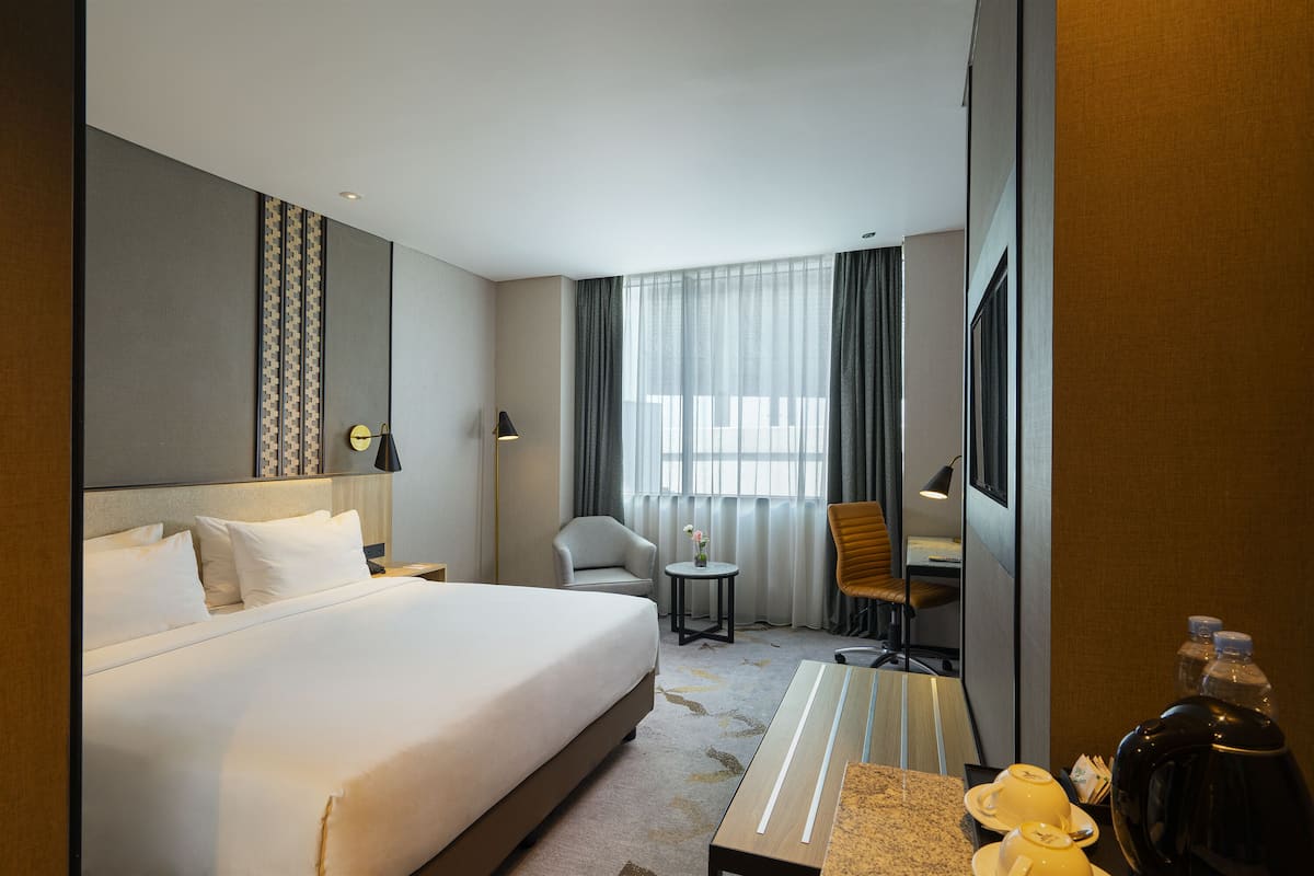 A hotel room with a large bed, a desk, a chair, a small table, and a TV.