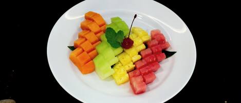 A white plate with neatly arranged fruit slices including orange, green, yellow, and red varieties, and a cherry on top.