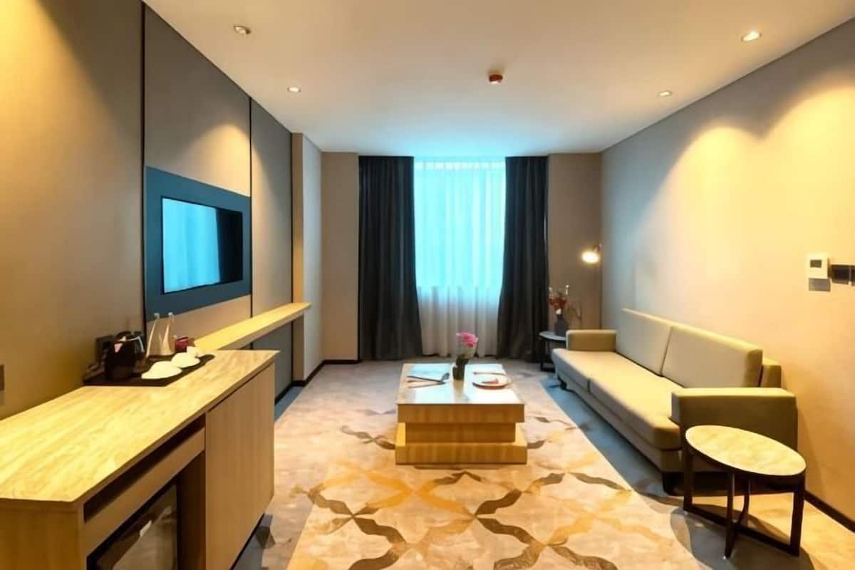 A hotel room with a wooden desk, a sofa, a small round table, and a TV mounted on the wall.