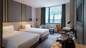A hotel room with two beds, a desk, a chair, a small table, and a large window. - Anara Airport Hotel (Tangerang)