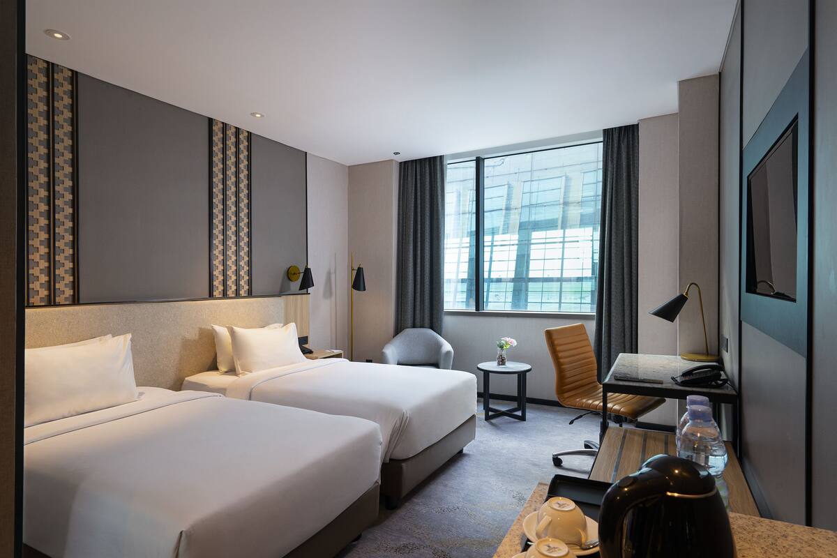 A hotel room with two beds, a desk, a chair, a small table, and a large window.