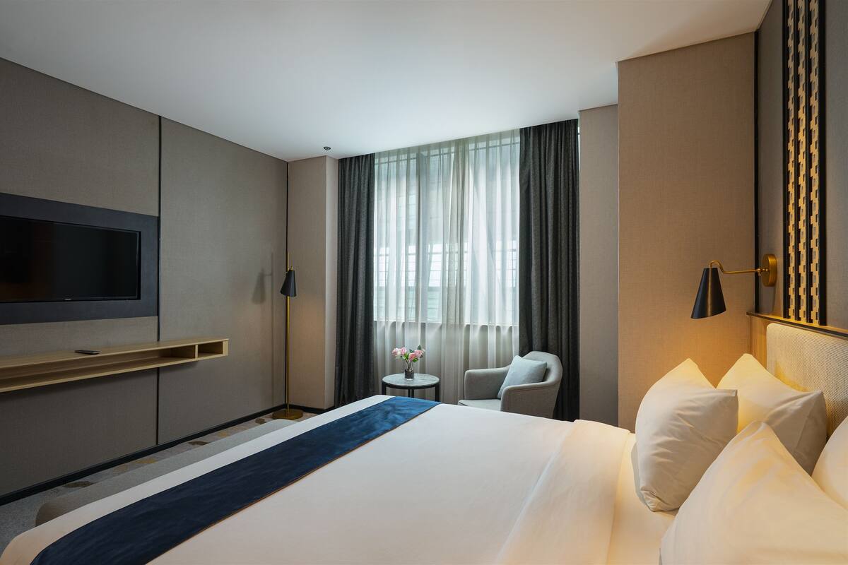 A hotel room with a large bed, a TV mounted on the wall, a small table with a vase of flowers, and a chair.