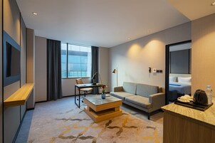 A modern hotel room with a sofa, a coffee table, a desk, and a TV.