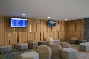 A modern hotel lobby with a large screen displaying flight information, comfortable seating areas, and a patterned carpet.