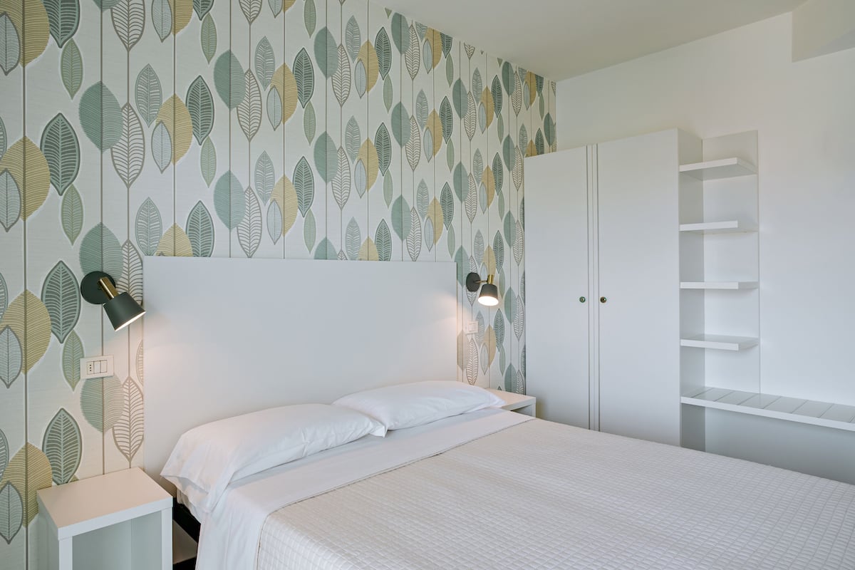 A bedroom with a bed, nightstands, a wardrobe, and a wall with leaf-pattern wallpaper.