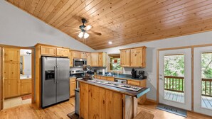 Una cocina amplia con gabinetes de madera, una isla central, electrodomésticos de acero inoxidable y ventanas grandes.